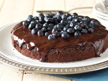 serving plate with a paleo blueberry chocolate cake topped with fresh blueberries and chocolate sauce