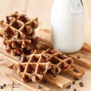 chocolate chip waffles stacked on a slotted tray with a jar of milk in the background