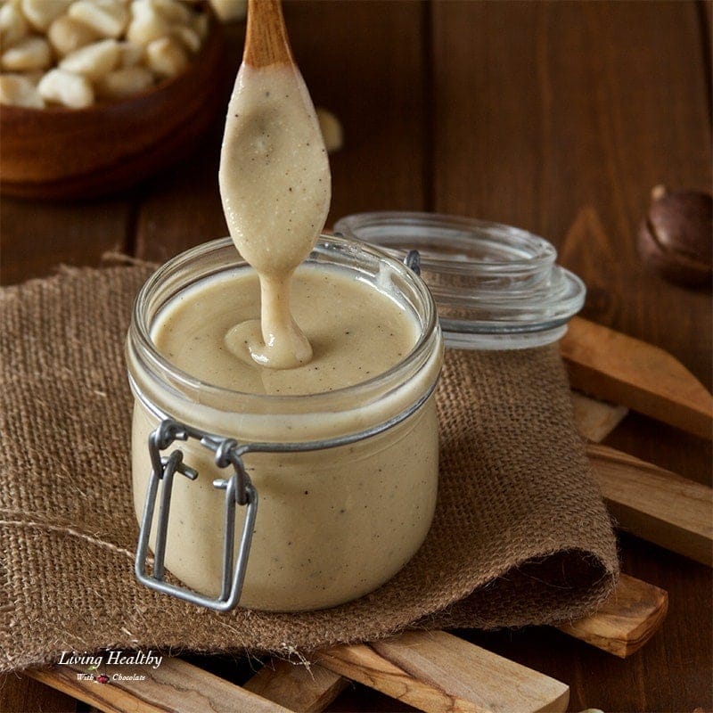 jar of homemade white chocolate macadamia nut butter with wooden spoon above dripping nut butter back into jar