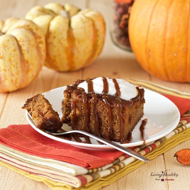 slice of paleo caramel pumpkin cake topped whipped cream drizzled in caramel and small decretive pumpkins in the background