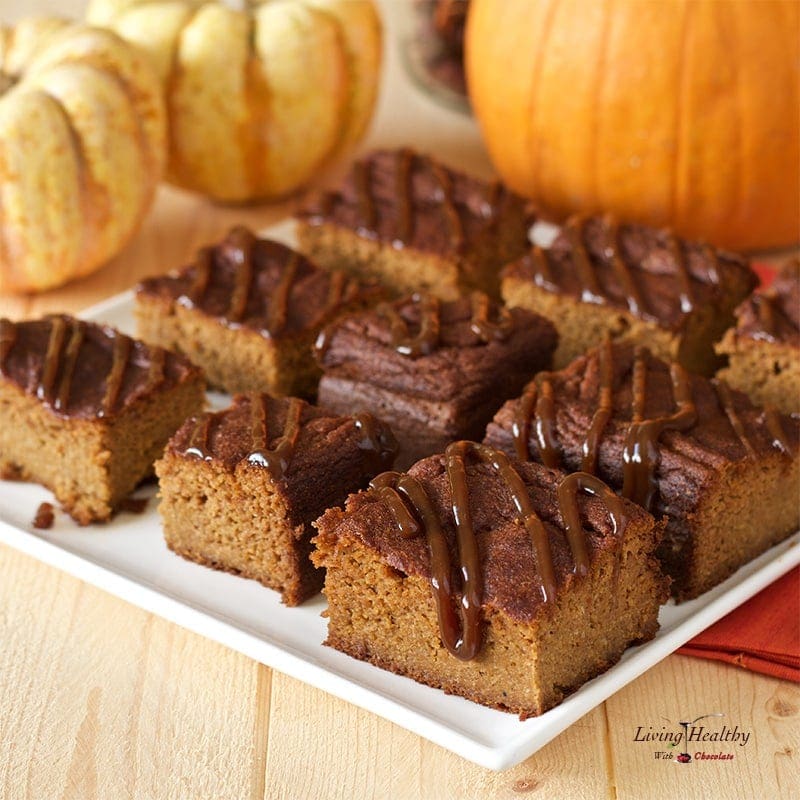 plate with cut squares of paleo marble pumpkin cake drizzled in homemade caramel and small Pumpkins in background 