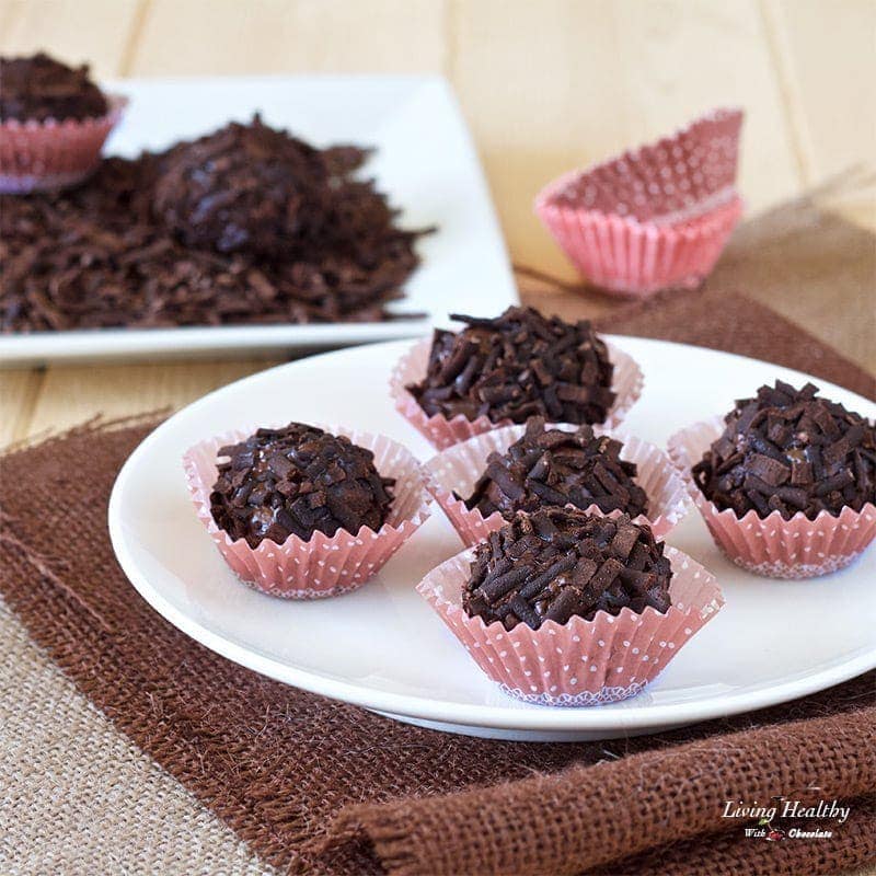 dark chocolate truffles in small paper cups with plate of chocolate in background 