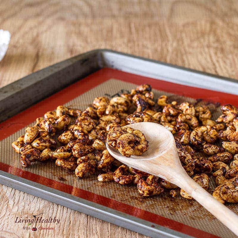 paleo cinnamon sugar candied cashews cooling on a baking sheet with silicone with a wooden spoon 