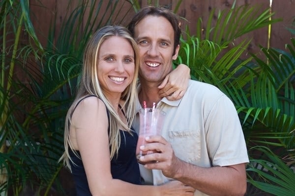 Adriana Harlan stojąca obejmując ramieniem męża Chucka przed zieloną palmą.
