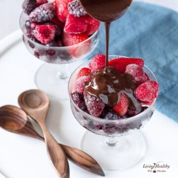two glass dishes with frozen berries and two wooden spoons with one dish of berries having chocolate poured over top