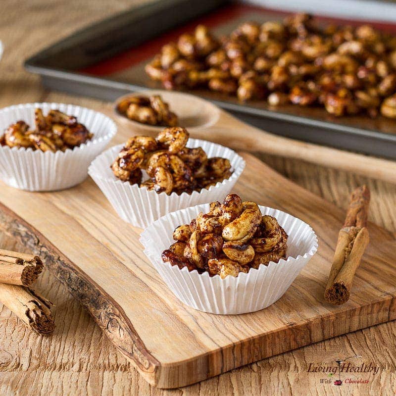 wooden cutting board display with cupcake holders filled with cinnamon sugar cashews and a tray of more nuts cooling behind