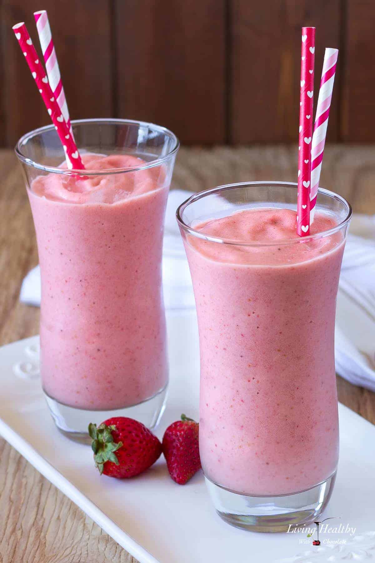 two glasses of dairy free paleo strawberry milkshakes served on white glass tray with a few loose strawberries