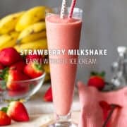 tall glass on a coaster filled with strawberry milkshake with two straws and some fresh fruits on the background.