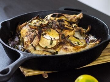 cast iron pan filled with roasted cinnamon lemon chicken topped with slices of lemon and caramelized onion