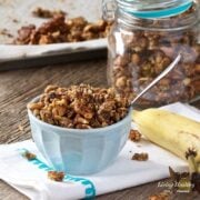 bowl of banana granola with jar of granola in background and banana on right side of bowl