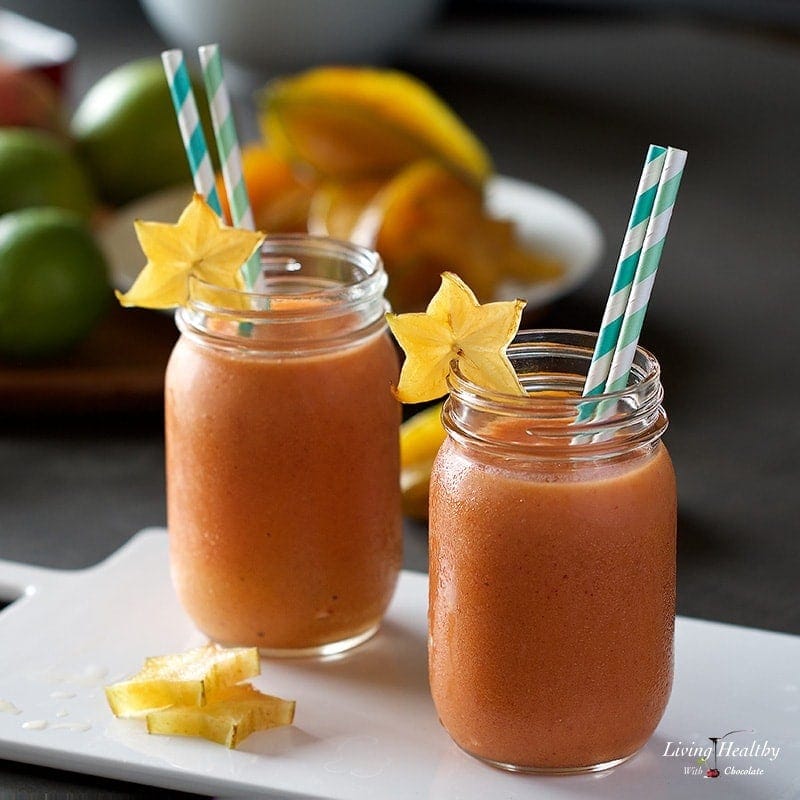 two jars filled with mango star fruit smoothie and decorated with slices of star fruit and two straws in each jar