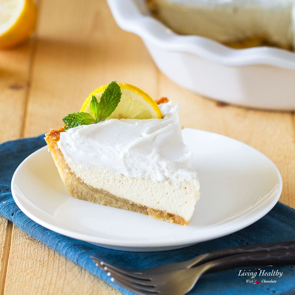 a slice of lemon cream pie on a white plate with blue napkin and pie dish in the background