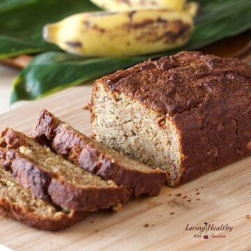 loaf of paleo banana bread on a cutting board with bananas in the background