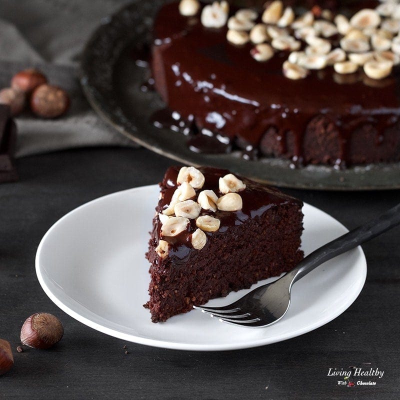 a piece of chocolate cake topped with hazelnuts on a white plate with a fork next to it
