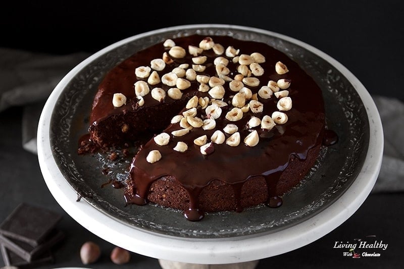 A chocolate cake on a plate topped with hazelnuts and drizzled with chocolate sauce