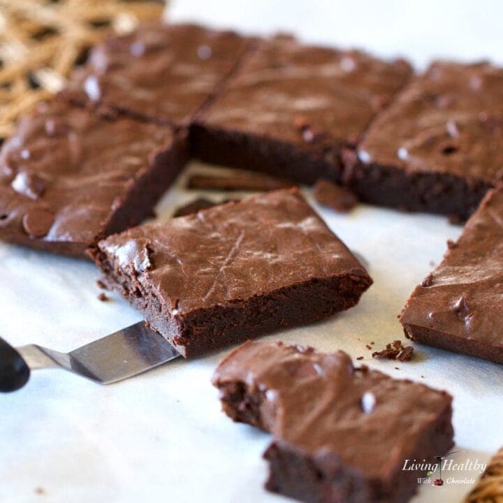 fudgy brownies cut into squares on parchment paper with one in the foreground with bite taken out