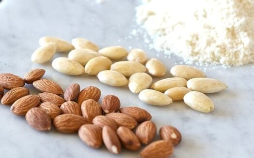 two piles of almonds and one pile of almond flour on a marble table