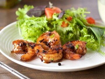 plate of cracked pepper shrimp and salad on wooden table with fork