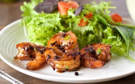 plate of cracked pepper shrimp and salad on wooden table with fork