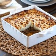 Shepherds pie in white serving dish sitting on wicker placemat with square section of pie removed