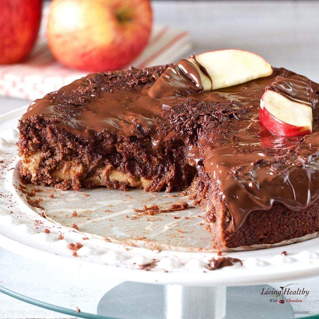 Apple chocolate cake with large slice cut out and apples on napkin in background