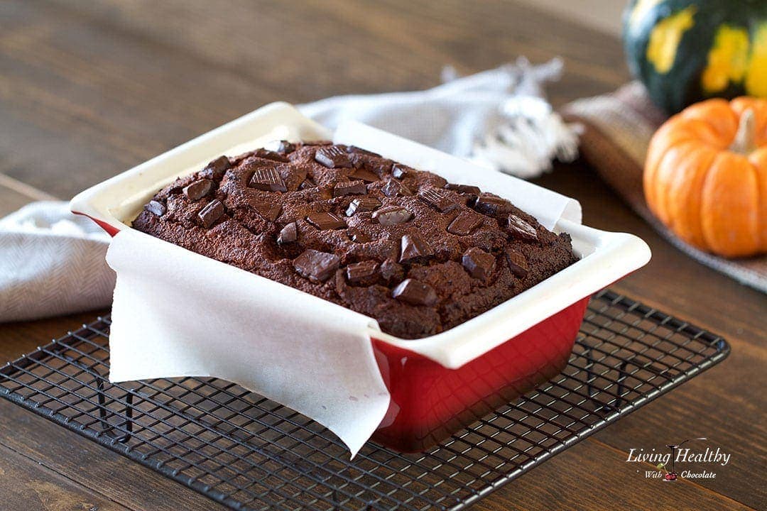 a loaf of chocolate pumpkin bread in a red baking dish fresh out of the oven cooling on a cooling rack