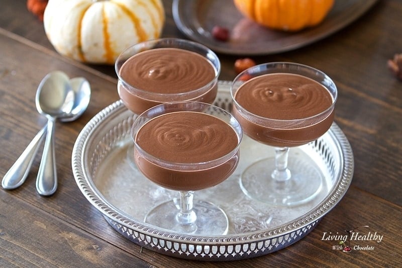 three dishes of pumpkin chocolate mousse on a silver serving platter with two small pumpkins in the background