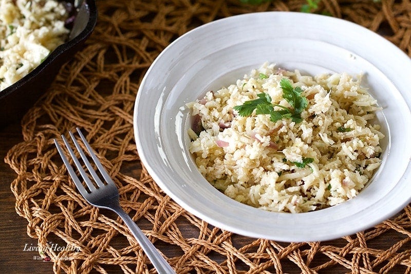 close up of cauliflower rice with cilantro on a place mat with a fork on the left side of the bowl