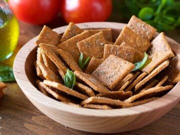 A bowl of crackers made with cassava flour on a table with tomatoes, olive oil and basil in the background