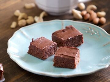 three pieces of no bake brownies on a plate with small piles of nuts and a glass of milk in the background