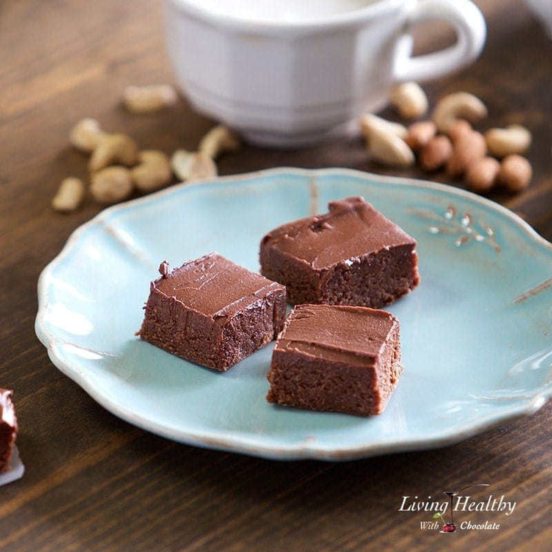 three pieces of no bake brownies on a plate with small piles of nuts and a glass of milk in the background