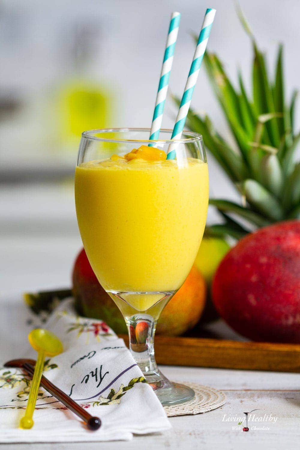 A close up of a mango smoothie with a plate of pineapple and mango behind