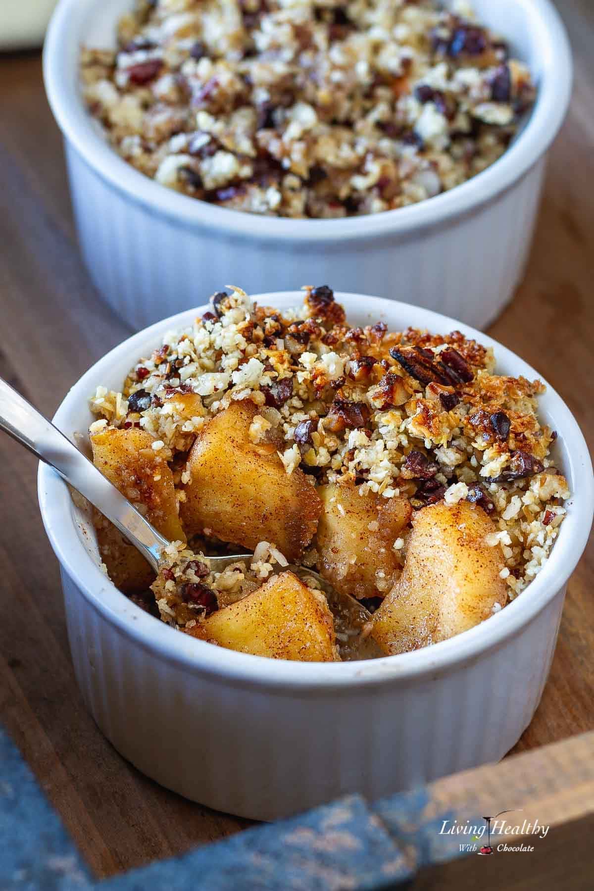 Two ramekins in a tray with apple crisp and spoon.