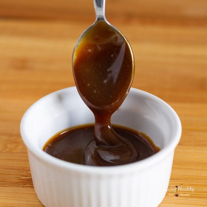 close up of a small white dish filled with homemade Caramel sauce with a spoon dripping sauce from above