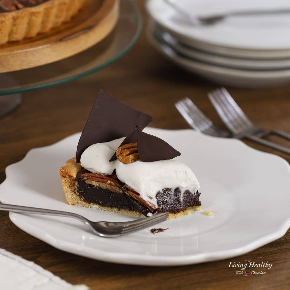 A slice of Chocolate Pecan Pie on a serving plate topped with Whipping cream and chocolate triangles