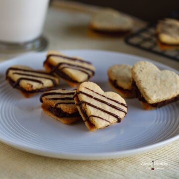 heart shaped vanilla sandwich cookies with chocolate filling inside and a drizzle of chocolate on top