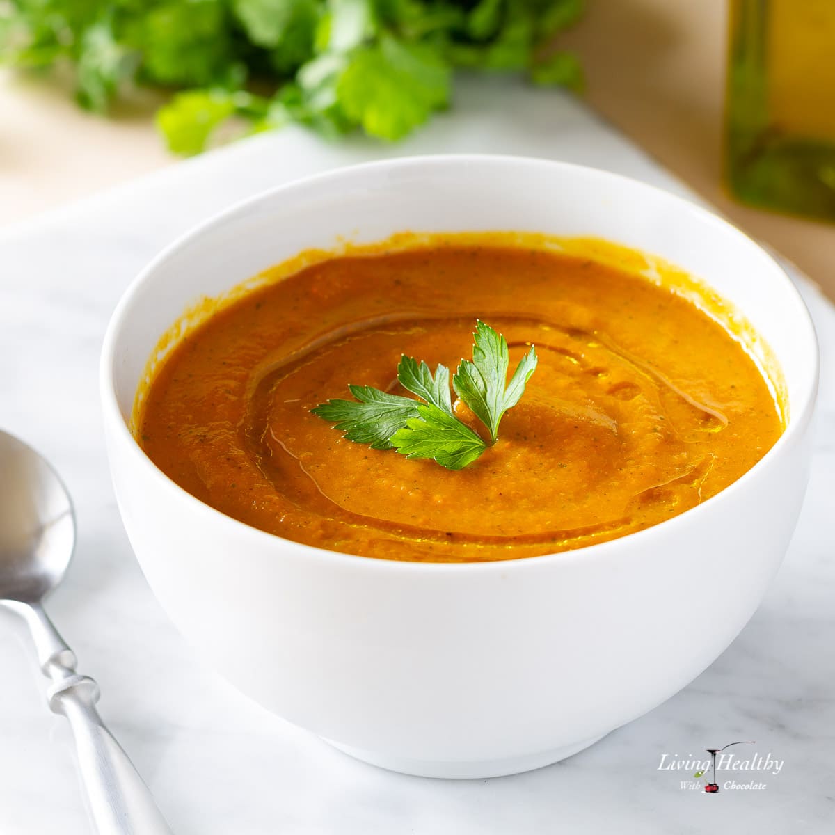 white bowl of carrot apple soup garnished with a leaf of parsley