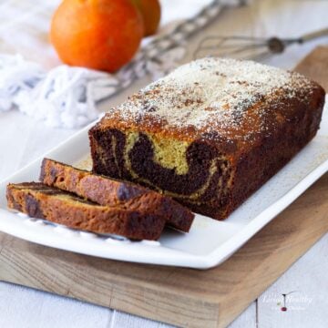 loaf of paleo orange marble cake on a plate with two cut slices and oranges in background