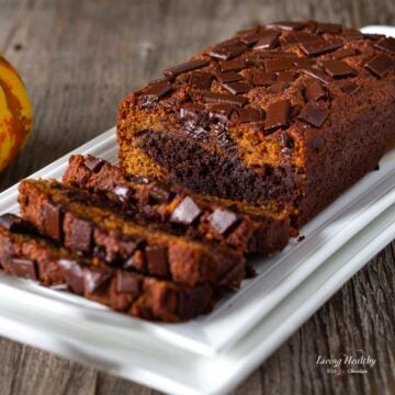 loaf of paleo marble pumpkin bread topped with chocolate chunks on serving plate with three slices cut out.