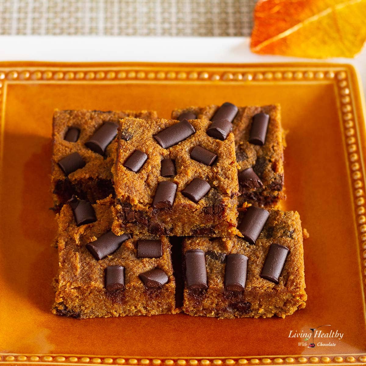 orange plate stacked with five pumpkin bars topped with chocolate chunks