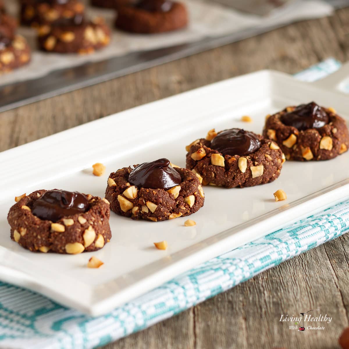 four hazelnut cookies in narrow white plate and a baking sheet ion the background with more cookies cooling.