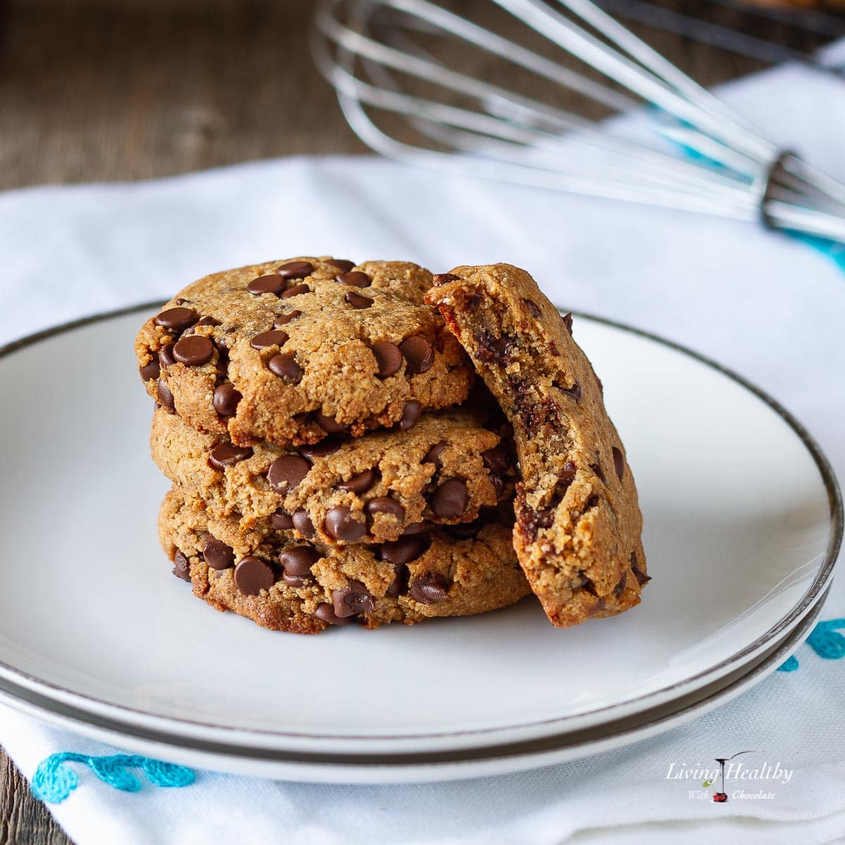 three chocolate chip cookies stacked on a white plate with another cookie with a bite taken off leaning on them