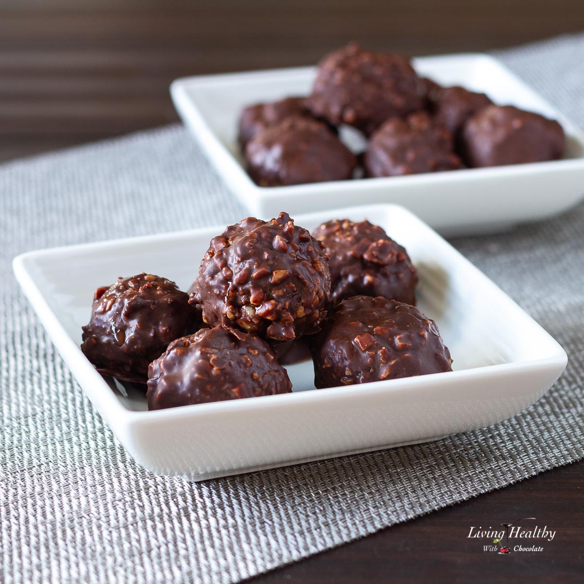 two small white serving dishes filled with several homemade Ferrero Rocher balls on a wooden table with silver placemat