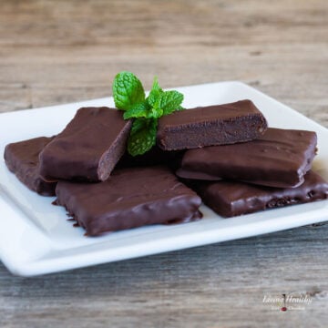 plate of chocolate covered thin mint fudge brownies garnished with a leaf of mint on a wooden table