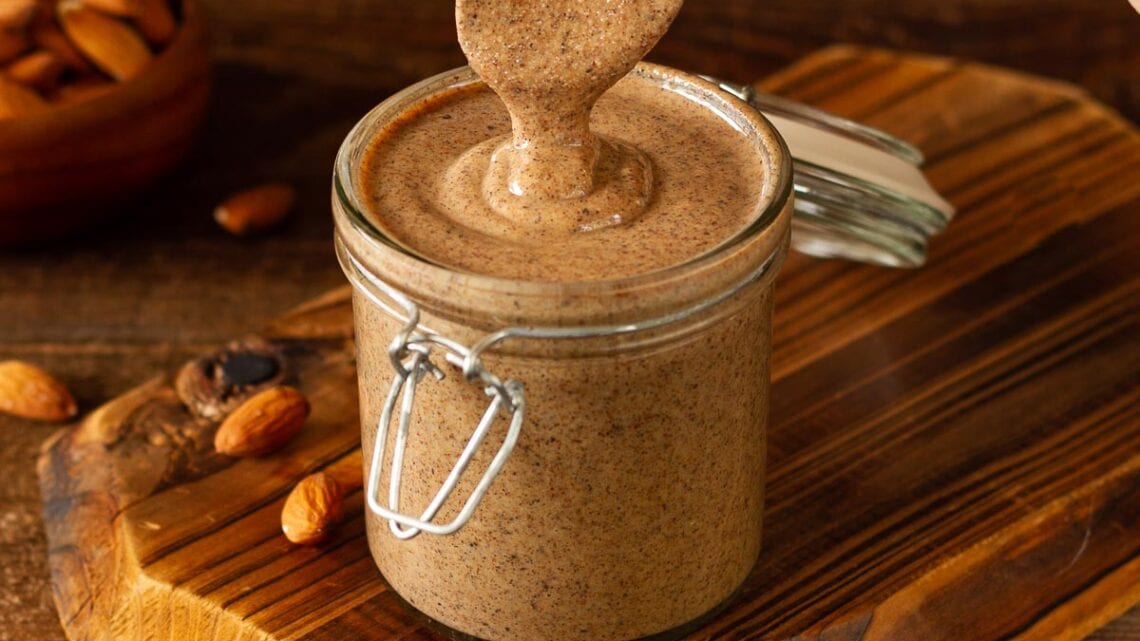 spoon dipped in a glass jar with homemade almond butter