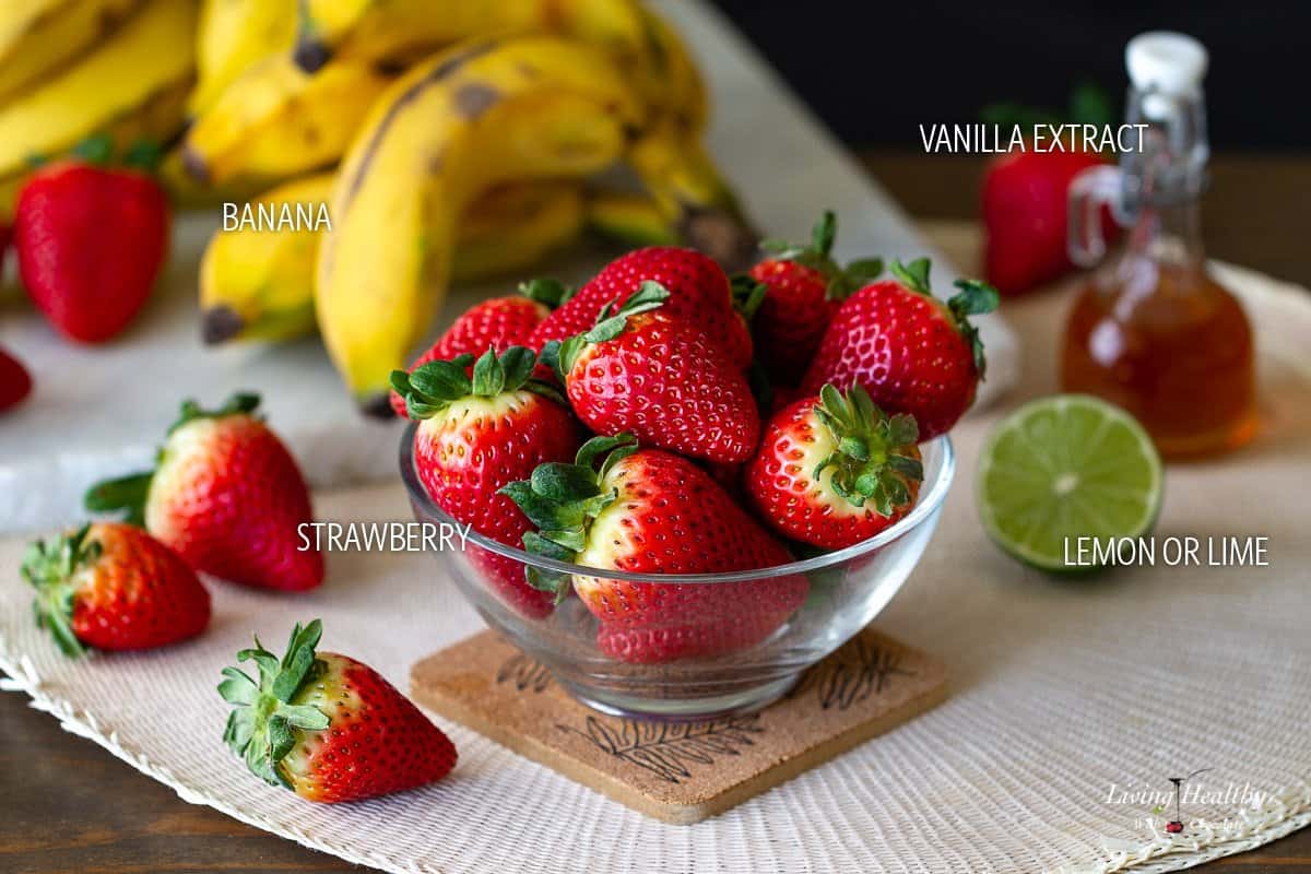 clear bowl on a table filled with strawberries, some bananas, a lime and a bottle of vanilla extract on the background.
