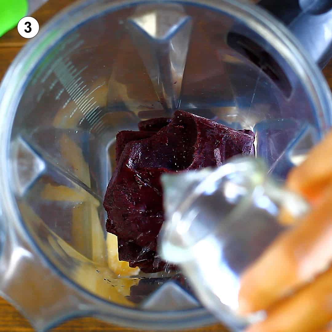 female hand pouring water from a glass into a blender containing banana and frozen acai puree