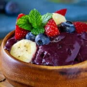 round wooden bowl filled with acai and topped with fresh banana blueberries and strawberries on a bamboo placemat